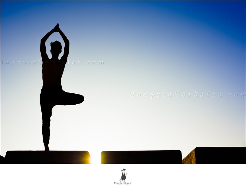 Silhouette Of A Man Practicing Yoga, Isolated Against The Blue Sky.